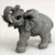 A detailed grey miniature elephant figurine, suitable for a bonsai tree display. The small elephant is captured in a dynamic pose with its trunk raised high and curled back towards its head, its mouth slightly open as if trumpeting. The figurine features realistic textures mimicking the wrinkled skin of an elephant, with large fan-like ears, sturdy legs, and small off-white tusks protruding from its face. Its dark eyes and intricately carved details add a lifelike quality. The figurine is set against a plain light-colored background, emphasizing its grey color and textured surface.