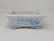 A 7-inch rectangular white ceramic Yixing bonsai pot featuring traditional blue painted designs. On its side, a framed blue landscape scene depicts a serene setting with rolling hills, a small pagoda-style building, and birds in flight. The pot's top rim is finished with a delicate blue border, and its four small feet are accented with a blue lattice design. This shallow, glazed bonsai pot is designed for displaying small bonsai trees, offering a classic blue and white aesthetic for collectors.