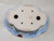 A detailed bottom view of a 10-inch painted Yixing bonsai pot, revealing its decorative and functional features. The pot has a distinctive lobed, cloud-like oval shape. The exterior is finished in a pale blue glaze with a delicate crazing or crackle pattern. Visible along the flared rim is a hand-painted landscape scene featuring charcoal-grey craggy mountains, a vibrant red setting sun, and several lines of black Chinese calligraphy. The flat, unglazed ceramic base is light cream in color and designed with practicality in mind, featuring two large primary drainage holes and four smaller auxiliary holes to ensure proper soil aeration. Centrally located on the bottom are authenticating marks: a faint, embossed square seal and a prominent handwritten artist's signature or kiln mark in reddish-brown pigment. This perspective highlights the craftsmanship involved in creating a high-quality Yixing ceramic piece intended for bonsai cultivation.