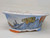 A 10-inch hand-painted Yixing ceramic bonsai pot featuring a traditional landscape scene. The pot has a lobed, oval shape with a wide, flared rim and short, rounded feet painted in orange and blue. The exterior depicts stylized light blue mountains with fine, dark line work for texture against a pale blue-white background. In the foreground, a prominent tree with bright yellow foliage is decorated with small black teardrop shapes. To the right, another tree has reddish-orange foliage with a scale-like pattern. Small black brush-stroke trees are scattered throughout the mid-ground. A decorative border of blue wavy lines and red dots runs along the top rim. The glaze has a delicate crazing or crackle effect, adding a vintage feel to the piece. Vertical black characters, likely a signature, are visible on the far left side.
