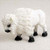 A detailed miniature figurine of a white buffalo, specifically designed as a decorative accessory for bonsai tree landscapes. The small bison is captured in a standing pose, facing slightly downward and to the left. Its entire body is covered in a highly textured, off-white finish that realistically mimics thick, shaggy winter fur, particularly around its large shoulder hump and head. Contrasting with its white coat, the figurine features solid black hooves and a dark black muzzle. This miniature animal adds a sense of scale and storytelling when placed at the base of a bonsai tree or within a miniature fairy garden scene.