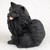 A detailed miniature figurine of a solid black Pomeranian dog, designed as a charming decorative accent for bonsai tree displays or indoor gardens. The figurine captures the dog in a sitting position, facing slightly to the left with a cheerful expression. It features intricate, deeply carved textures that realistically mimic the Pomeranian's characteristic thick, fluffy coat and long fur. The dog has small, alert, pointed ears, dark shining eyes, and a tiny pink tongue sticking out of its slightly open mouth. The entire piece is rendered in a matte black finish and is photographed against a neutral, light-colored background to highlight its silhouette and fine details as a pet-themed accessory.