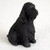A detailed miniature figurine of a solid black English Cocker Spaniel, specifically designed as a decorative accent for bonsai trees and miniature landscape displays. The figurine depicts the dog in a classic sitting pose, looking attentively to the side. Its design emphasizes the breed's characteristic features, including long, drooping ears with deeply textured, wavy fur details that cover its entire body. The craftsmanship captures the essence of an English Cocker Spaniel, with subtle highlights on its dark eyes and nose. This small black figurine is showcased against a soft, off-white textured background, highlighting its intricate molding. Perfect as a bonsai tree companion, this English Cocker Spaniel figurine adds a unique and personalized element to botanical arrangements.