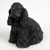 A detailed miniature figurine of a black Cocker Spaniel in a sitting pose, facing slightly to the left. The figurine captures the breed's distinctive long, wavy ears and textured, curly coat in a solid matte black finish. This small animal figure is intended as a decorative accessory for a bonsai tree or miniature garden, shown here against a plain off-white background.