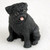A detailed, miniature black pug figurine designed as a decorative accessory for a bonsai tree or terrarium. The small sculpture depicts a pug sitting upright on its haunches, looking alert and cheerful. Its deep black coat features a realistic textured finish mimicking short fur, especially around its wrinkled face and sturdy legs. The pug has classic breed characteristics, including a flat muzzle, small folded ears, and large, dark, shiny eyes that look slightly off-camera. Its mouth is partially open in a happy expression, revealing a small, soft pink tongue sticking out. The figurine is set against a simple, light-colored background, emphasizing its compact size and intricate craftsmanship for bonsai enthusiasts.