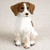 A detailed miniature figurine of a Brittany Spaniel dog, designed as a decorative accessory for a bonsai tree or miniature garden. The figurine depicts the spaniel in a sitting pose, looking slightly to the side. Its coat is primarily white with classic liver-brown markings, including long, floppy brown ears and patches around its dark, soulful eyes. A distinct white blaze runs down the center of its face to a small black nose. The sculpture features a textured finish to mimic the appearance of fur, with subtle light-brown ticking or spots on its white front legs and paws. The figurine stands on a neutral, off-white surface, highlighting its craftsmanship as a charming addition to a botanical display.