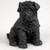A detailed matte black figurine of a Shar-Pei puppy, depicted in a sitting position. The miniature sculpture intricately captures the breed's characteristic deep skin folds and heavy wrinkles across its entire body, especially concentrated around the head, neck, and shoulders. It features a broad muzzle, small triangular ears that fold forward, and large, dark, glossy eyes that catch the light. The uniform black color of the figurine is set against a neutral, light-colored background, highlighting its texture and form as a decorative accessory for a bonsai tree arrangement.