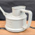 This close-up product photo showcases a light grey, matte plastic Tinyroots watering can, specifically designed for precise bonsai tree care. The watering can has a cylindrical body with the brand name "tinyroots" embossed on a rectangular plaque on its side. It features a wide, oval-shaped opening at the top for easy filling and a thick, rectangular handle on one side for a comfortable and stable grip. A long, thin spout, essential for reaching through dense bonsai foliage, is partially visible extending from the opposite side. The watering can is positioned on a light brown wooden surface with a striking dark grain, set against a textured dark grey backdrop, highlighting its simple and functional design.