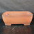 An eye-level, full-view shot displays a 14-inch rectangular unglazed Yixing bonsai pot (model YX1094), highlighting its classic design and warm, reddish-brown terracotta color. The pot features smooth, gently sloping sides that taper slightly toward the base, finished with rounded corners and a clean, slightly flared rim. A subtle decorative ridge runs along the lower perimeter, just above four sturdy, integrated block feet that provide essential elevation for drainage and air circulation. The matte, fine-grained texture of the authentic Yixing clay is visible under soft, diffused lighting. The vessel is centered on a dark, reflective surface against a matte black background, emphasizing its elegant proportions and earthy, natural aesthetic.