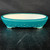A 12-inch oval Yixing ceramic bonsai pot featuring a vibrant teal glazed finish. The exterior is decorated with a pattern of small, raised rivets or studs along the lower half, adding a textured, antique-inspired detail to its glossy surface. The pot has a shallow, wide profile with a contrasting cream-colored unglazed interior. It sits on four elegant, slightly curved feet and is displayed on a dark, textured wooden surface against a black background, highlighting its rich color and craftsmanship.