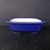 A 9-inch blue glazed square Yixing ceramic bonsai pot, model number 2281C, is shown centered against a dark, minimalist background. The pot features a vibrant, glossy royal blue glaze on its exterior and a contrasting smooth, off-white glazed interior. Its shape is a deep rectangular basin with elegant, indented corners and a wide, flat rim that flares slightly outward. The vessel sits on four small, integrated corner feet that elevate it slightly from the dark, wood-textured surface below. The clean lines and traditional ceramic craftsmanship of the pot are highlighted by soft lighting, emphasizing its glossy finish and classic design, suitable for a variety of bonsai tree styles.