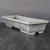 A professional studio photograph of an 11-inch unglazed Yixing bonsai pot, showcasing its minimalist and elegant design. The pot is rectangular and shallow, crafted from a fine-grained, matte gray clay that exhibits subtle, natural tonal variations across its surface. It features a distinct, flat rim around its top edge and is supported by four sturdy, block-style feet with small arch-shaped cutouts designed for stability and drainage. The pot is shown from a three-quarter perspective, highlighting both its interior space and exterior form. It sits on a dark, textured wooden surface against a solid, dark gray background, which focuses attention on the pot's clean lines and earthy, unglazed texture.