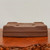 An eye-level studio photograph shows a 9-inch unglazed rectangular Yixing bonsai pot, item number 2288a from Bonsai Outlet, positioned upside down to showcase its bottom. The pot is crafted from a high-quality, fine-grained clay in a deep, matte reddish-brown color, characteristic of authentic Yixing pottery. 

The underside of the rectangular pot reveals two large, clean-cut circular drainage holes and four smaller wire holes located near the corners, which are used to secure a bonsai tree in place. The sides of the pot feature a refined, two-tiered design with a subtle horizontal groove running around the circumference near what would be the base. The pot rests on a polished, natural-edged wooden display stand with a rich grain, providing a warm contrast to the earthy clay. The entire scene is set against a plain, off-white background, highlighting the classic form and functional details of this traditional bonsai container.