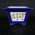 An 8-inch blue square Yixing bonsai pot is showcased against a dark, textured background. The ceramic vessel features a vibrant, deep cobalt blue glaze covering its flared rim, frame, and tapered body. In the center of the front face is a recessed white rectangular panel decorated with traditional hand-painted black ink Chinese calligraphy in a fluid, cursive style. Small red ink seals flank the script, adding a touch of classic detail. The pot rests on four small, integrated feet, giving it a stable and elevated profile. This handcrafted Yixing pot combines elegant ceramic artistry with functional design, making it a striking choice for displaying a bonsai tree.