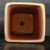 A top-down interior view of a square, tall cascade-style Yixing bonsai pot. The pot has a thick, light cream-colored glazed rim that provides a sharp contrast to the rich, unglazed reddish-brown terracotta interior.

At the bottom of the pot, a large, centered drainage hole is visible, flanked by four smaller, circular holes arranged in a square pattern, which are used for anchoring a bonsai tree with wire. The pot’s square shape features elegantly rounded corners. On the upper inside rim, the model number "1785 D" is handwritten in thin white characters. The pot is photographed against a dark background, resting on a dark, slightly reflective surface that highlights its solid construction and deep profile, typical of high-quality Yixing pottery designed for cascade bonsai styles.