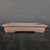 A wide-angle, eye-level shot showcases a 14-inch unglazed rectangular Yixing bonsai pot, model No. 2463-1. The pot is crafted from traditional Yixing clay, exhibiting a rich, earthy, reddish-brown or terracotta color with a smooth, matte finish. 

The pot's design is classic and elegant, featuring a shallow, rectangular form with side walls that curve slightly inward. A prominent, wide rim flares gently outward at the top. The base is supported by four integrated, low-profile block feet situated at each corner, providing stability and allowing for essential drainage. 

Centrally positioned on a dark, subtly textured black surface that resembles wood grain, the pot stands out against a plain, dark charcoal background. The minimalist setting highlights the pot's clean lines and high-quality ceramic craftsmanship, making it a perfect container for various bonsai tree styles.