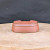 A detailed, eye-level photograph of a 4.5-inch unglazed oval Yixing bonsai pot, shown upside down on a light-toned, rustic circular wooden platform. The pot is made from smooth, reddish-brown clay with a fine-grained texture and features a subtle horizontal ridge around its body. In this inverted position, the bottom of the pot is clearly visible, showcasing several pre-drilled drainage and wire holes necessary for proper tree care, along with a faint rectangular maker's mark in the center. The warm, earthy tones of the terracotta pot contrast sharply against a dark, textured gray background, emphasizing its clean silhouette and traditional craftsmanship.