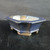 A high-angle, three-quarter view of a 7-inch glazed Yixing bonsai pot with an elegant octagonal shape. The ceramic pot features sides that slope outward from a stepped base to a wide, flat rim. Its exterior is finished with a glossy, deep blue glaze that has subtle texture and color variations, creating a rich and classic appearance. The interior and the four small, rectangular feet are unglazed, revealing the natural, light-tan color and fine texture of the Yixing clay. The pot is positioned on a dark, textured black surface against a neutral dark grey background, highlighting its structural design and vibrant blue color.
