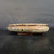 A wide-angle, eye-level shot of a 12-inch glazed Yixing bonsai pot, model number 1862J, resting on a dark-grained wooden surface. The shallow, oval ceramic pot features a rounded body with a glossy glaze in shades of pale sage green, with vertical ridges highlighted by streaks of rust-orange and dark brown. This mottled, earthy color palette gives the pot an aged, organic appearance. The pot has a slightly flared rim and is supported by four small, sturdy, integral feet. The scene is set against a plain, dark charcoal background, which creates a sharp contrast that makes the pot's rich colors and reflective, glazed texture stand out. The lighting is soft, creating gentle highlights on the smooth surfaces of the pot.