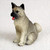 A detailed miniature figurine of a gray and buff Akita dog, designed as a decorative accessory for a bonsai tree display. The small, lifelike statue depicts the Akita in a sitting pose, alert and looking slightly to the side. Key breed characteristics are prominently featured, including its signature black muzzle, upright pointed ears, and a thick tail curled over its back. The figurine has a textured, fur-like appearance with realistic hand-painted details, and a tiny pink tongue is visible in its open mouth. This charming collectible is perfect for adding character and a sense of life to the landscape of a miniature bonsai garden.