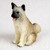 A small, detailed miniature Akita fawn dog figurine designed for bonsai tree decoration. The figurine shows a sitting Akita with a light tan, textured coat that mimics real fur. It features a dark black muzzle, small glossy black eyes, and a pink tongue peeking out in a cheerful, panting expression. Its pointy ears are alert with black accents, and its characteristic bushy tail is curled over its back. The figurine is set against a plain, off-white background, highlighting its realistic craftsmanship and charm as a decorative accessory for a miniature garden or bonsai display.