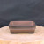 A detailed view of a rectangular Yixing clay bonsai pot, SKU 1157, presented on a rustic, light-colored wooden slab against a dark charcoal background. This unglazed ceramic planter features a unique two-tone finish, with a primary warm reddish-brown body that transitions into a dark, smoky charcoal color around the upper rim and at the base. The pot has smooth, rounded corners and a subtle horizontal ridge encircling its middle. It stands on four low, integrated block feet that share the dark finish of the rim. The interior is the same earthy brown as the exterior, showcasing the fine grain of the traditional Yixing clay.