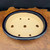 An overhead perspective of a premium 10.25-inch oval bonsai pot, masterfully created by Katsushi Kataoka under the Reiho name at the renowned Seizan Kiln. The pot is finished in a deep, lustrous dark blue glaze that coats the exterior and the flat, rounded rim, reflecting light with a brilliant shine. Inside, the pot remains unglazed, exposing the fine-textured, sandy-beige ceramic clay. 

Seven drainage holes are strategically placed across the bottom—one large central hole flanked by pairs of smaller holes—to facilitate optimal water drainage and soil aeration for a bonsai tree. A light, hand-etched maker's mark is visible in the center of the pot's floor. The pot is presented on a beautiful, highly polished burl wood slab with intricate grain patterns, set against a dark, minimalist background to emphasize its sophisticated Japanese design and artisanal craftsmanship.