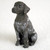 A detailed miniature figurine of a German Shorthaired Pointer puppy, designed as a decorative accessory for a bonsai tree or indoor garden. The figurine is shown in a classic sitting pose, looking alertly toward the left. Its head and soft, floppy ears are a solid dark liver-brown color, contrasting with its white body that is heavily "ticked" or mottled with matching brown patches, a hallmark of the breed. 

The small sculpture features realistic, textured fur-like detailing across its body and tiny, glossy black eyes that give it a life-like appearance. It sits on a plain, light-colored surface that emphasizes its intricate markings and compact size. This German Shorthaired Pointer bonsai tree figurine serves as a charming and realistic miniature companion for any bonsai display.