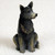 A detailed miniature figurine of an Australian Cattle Dog, often referred to as a Blue Heeler or Blue Dog, designed as a decorative accessory for a bonsai tree pot. The small resin figurine is shown in an alert, upright sitting position with its head turned slightly to the right and its pointed ears pricked. Its coat is primarily a dark blue-gray with intricate molded fur textures, featuring traditional tan markings on its muzzle, chest, and paws. A characteristic small white patch is visible on the top of its head. The figurine is photographed against a clean, neutral, off-white background, emphasizing its realistic features and small scale for use in miniature garden landscapes.