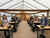 Group of bonsai workshop students seated at individual workstations inside a greenhouse classroom, each with a Jade bonsai tree, soil container, pot, tools, and supplies in front of them. The image shows the organized classroom layout, small-group learning environment, and hands-on workshop setup.