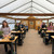 Group of bonsai workshop students seated at individual workstations inside a greenhouse classroom, each with a Jade bonsai tree, soil container, pot, tools, and supplies in front of them. The image shows the organized classroom layout, small-group learning environment, and hands-on workshop setup.