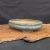An elegant, shallow, oval-shaped Yixing bonsai pot is showcased in a side-angle photograph. The ceramic planter features a glossy, sea-foam green glaze with a soft, reflective finish and subtle crazing. It has a classic double-lipped rim and a lobed silhouette, resting on four small, decorative cloud-style feet.