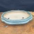 An elegant, shallow, oval-shaped Yixing bonsai pot is showcased in a side-angle photograph. The ceramic planter features a glossy, sea-foam green glaze with a soft, reflective finish and subtle crazing. It has a classic double-lipped rim and a lobed silhouette, resting on four small, decorative cloud-style feet.