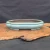 An elegant, shallow, oval-shaped Yixing bonsai pot is showcased in a side-angle photograph. The ceramic planter features a glossy, sea-foam green glaze with a soft, reflective finish and subtle crazing. It has a classic double-lipped rim and a lobed silhouette, resting on four small, decorative cloud-style feet.