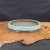 An elegant, shallow, oval-shaped Yixing bonsai pot is showcased in a side-angle photograph. The ceramic planter features a glossy, sea-foam green glaze with a soft, reflective finish and subtle crazing. It has a classic double-lipped rim and a lobed silhouette, resting on four small, decorative cloud-style feet.