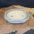 An elegant, shallow, oval-shaped Yixing bonsai pot is showcased in a side-angle photograph. The ceramic planter features a glossy, sea-foam glaze with a soft, reflective finish and subtle crazing. It has a classic double-lipped rim and a lobed silhouette, resting on four small, decorative cloud-style feet.