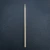 A minimalist, top-down photograph of a single wooden toothpick placed vertically in the center of a dark frame. The toothpick is made of light-colored wood with a smooth finish and a visible fine grain. Its top end tapers into a sharp point, while the bottom end features a small, decorative circular groove near the base. The background is a dark gray or black slate-like surface with a fine, irregular texture that provides a sharp contrast to the pale wood. The lighting is soft and even across the entire scene, highlighting the cylindrical shape of the toothpick without casting heavy shadows.