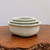 A set of three nested Japanese Tokoname bonsai pots, each featuring a smooth cream-glazed finish with a soft, satin sheen. The pots are rectangular with rounded corners, a design often referred to as a "mokko" or cushion shape. 

The pots increase in size from top to bottom, with the smallest tucked inside the medium, and both nestled within the largest. Each pot has a wide, flat rim that flares slightly outward, accented by a subtle, distressed edge where the darker clay body peaks through the off-white glaze. The largest pot at the base rests on four short, integrated feet. 

The entire set is showcased on a rustic, textured reddish-brown wooden surface, likely a cross-section of a tree trunk or burl, which provides a natural contrast to the clean, elegant lines of the ceramic. The background is a solid, neutral light gray, keeping the focus entirely on the craftsmanship of the traditional Japanese pottery.