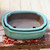 A close-up, slightly high-angle shot showcases two nested, high-quality Japanese bonsai pots from Tokoname. The pots feature a vibrant, glossy teal Oribe glaze on the exterior and along the scalloped rim, which beautifully contrasts with the unglazed, matte brownish-gray interior and base. Both pots have a traditional mokko-style shape, characterized by a rectangular form with soft, rounded, and indented corners. 

Inside the top pot, two large drainage holes are clearly visible. The set rests on a distressed, rustic wooden surface with peeling red and white paint, which adds a textured, aged feel to the composition. The background consists of softly blurred, light-colored vertical wooden planks, ensuring the focus remains entirely on the craftsmanship and color of the authentic Oribe-glazed bonsai containers.