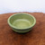 A 7-inch round Yixing glazed succulent dish, model No. 844, sits centered on a polished dark brown wooden surface with an intricate burl grain. The ceramic bowl features a wide, thick rim and small, integrated feet at its base. It is covered in a beautiful, mottled green glaze that has a speckled, almost crystalline texture, with varying shades of lime and deep forest green. The interior of the bowl shows the same vibrant, textured glaze. This artisanal pot, which contains no drainage holes, is set against a clean, stark white background, emphasizing the rich color and handcrafted quality of the glazed stoneware, commonly used in bonsai and succulent cultivation.