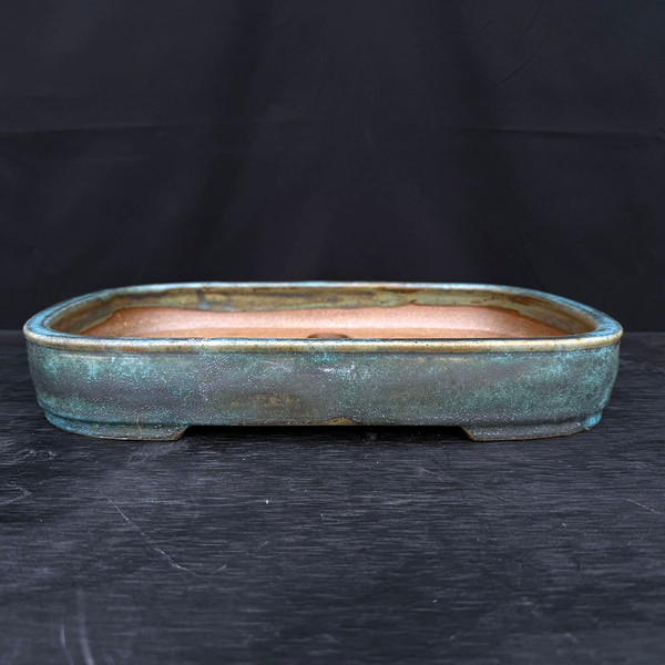 A professional, 15-inch handmade ceramic bonsai pot by artist Jack Hoover, designated as No. 603. The shallow, rectangular container features soft, rounded corners and a rich, heavily textured glaze. The glaze displays a complex, mottled appearance with primary shades of turquoise and weathered teal, accented by earthy brown and dark charcoal grey undertones, creating an antique, oxidized copper patina.

The pot’s interior reveals a natural, unglazed warm tan clay finish, with a central drainage hole visible at the bottom. It sits on low, integrated corner feet that provide a slight lift. The pot is centered on a dark, horizontally grained wooden surface against a solid black background, emphasizing its artisanal craftsmanship and unique color palette.