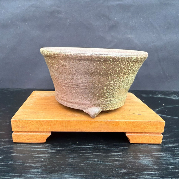 Side profile of Kakuzan Tokoname round bonsai pot with rustic brown speckled finish, flared rim, and three feet on a display stand