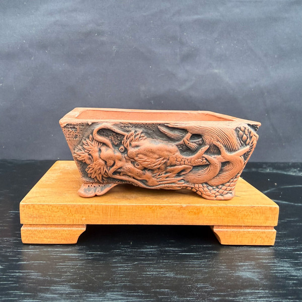 Front view of Kouji Watanabe Tokoname rectangle bonsai pot showing carved dragon relief on unglazed red clay and sculpted feet