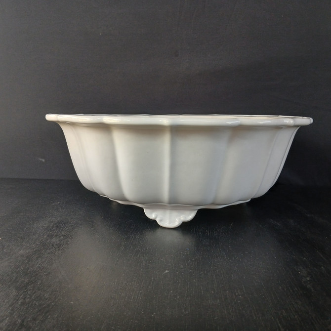 A detailed side profile of a 17-inch white round glazed Yixing bonsai pot, showcased against a stark, dark gray background and a matte black surface. This high-quality ceramic pot features a brilliant, glossy white finish that catches the light along its elegant curves. Its body is designed with deep, vertical fluting or lobing that flares outwards, leading to a decorative scalloped rim with a gentle, wavy edge. The pot sits on ornate, cloud-style feet that add a touch of traditional craftsmanship to its sturdy base. The clean, minimalist aesthetic of the white glaze provides a beautiful contrast, making it an ideal vessel for showcasing the vibrant greens of a bonsai tree.