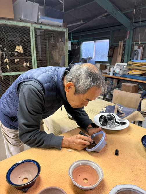Kakuyuki Watanabe (Kakuzan) signing a Tokoname bonsai pot at Kakuzan Toen kiln workshop, behind-the-scenes studio photo