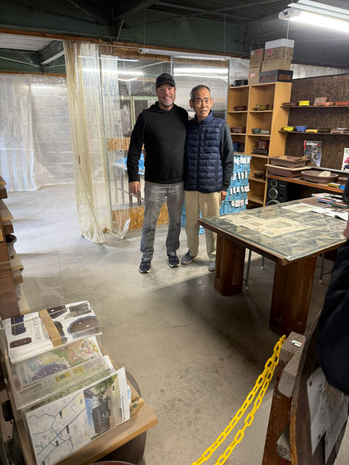 Visitor photo inside Kakuzan Toen Tokoname workshop with Kakuyuki Watanabe (Kakuzan) surrounded by bonsai pots and shelving