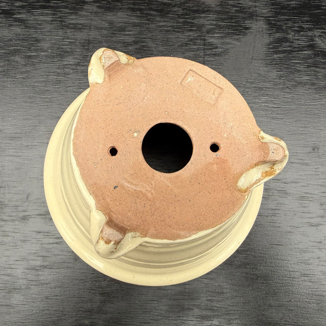 Underside of Kakuzan Tokoname bonsai pot showing three feet, drainage hole, tie-down holes, and artist stamp on clay base