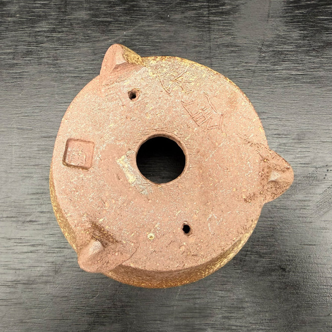 Underside of Kakuzan Tokoname bonsai pot showing three feet, drainage hole, tie-down holes, and artist marks on clay base