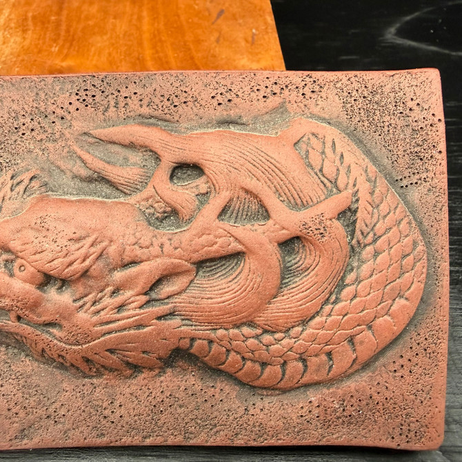 Close-up of Tokoname dragon plaque showing carved dragon body and scale detail with darkened firing contrast