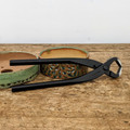 A high-quality pair of black carbon steel Tinyroots concave cutters lies prominently across a rustic, weathered wooden work surface. These professional-grade bonsai tools, featuring long, ergonomic handles and a sharp, rounded cutting head, are essential for making clean, flush cuts that heal smoothly on branches. The "Tinyroots" brand name is clearly embossed on the matte black handle near the heavy-duty pivot point. In the background, two small, decorative ceramic bonsai pots provide context; one is a shallow, green-glazed oval pot with visible drainage holes, and the other is a rounder pot with a textured brown and green finish. The scene, set against a simple, clean white background, showcases the specialized equipment found in the Tinyroots Ultimate Carbon Steel Tool Kit, making it an ideal visual for bonsai enthusiasts and practitioners looking for high-performance pruning tools.